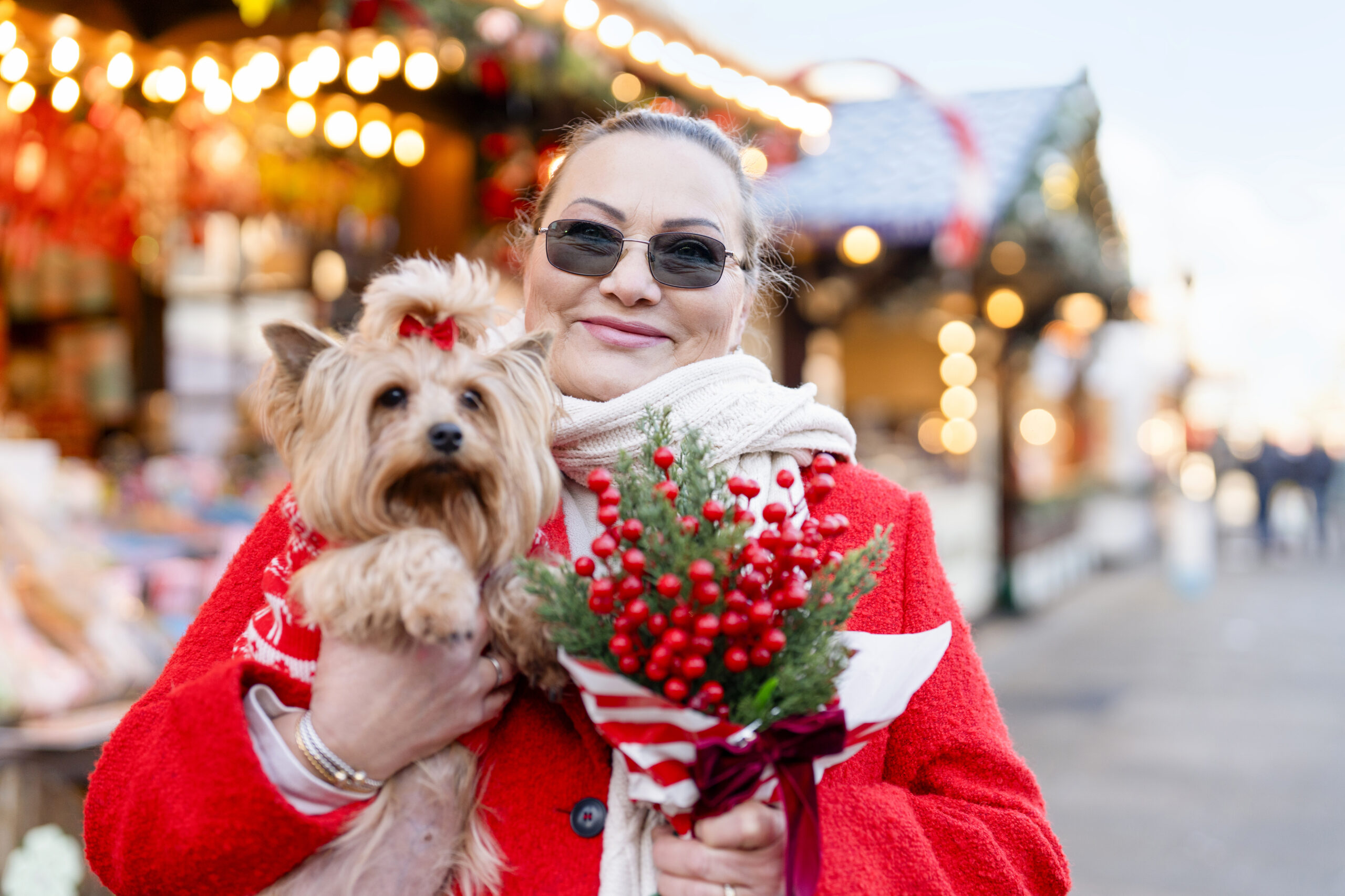 Woman holding a small dog and a bouquet at a festive market during the holiday season